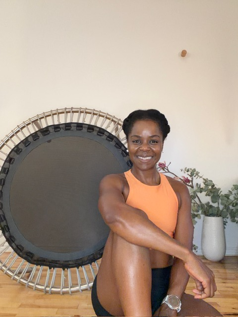 Dani sitting beside her fitness trampoline in a warm-lit studio